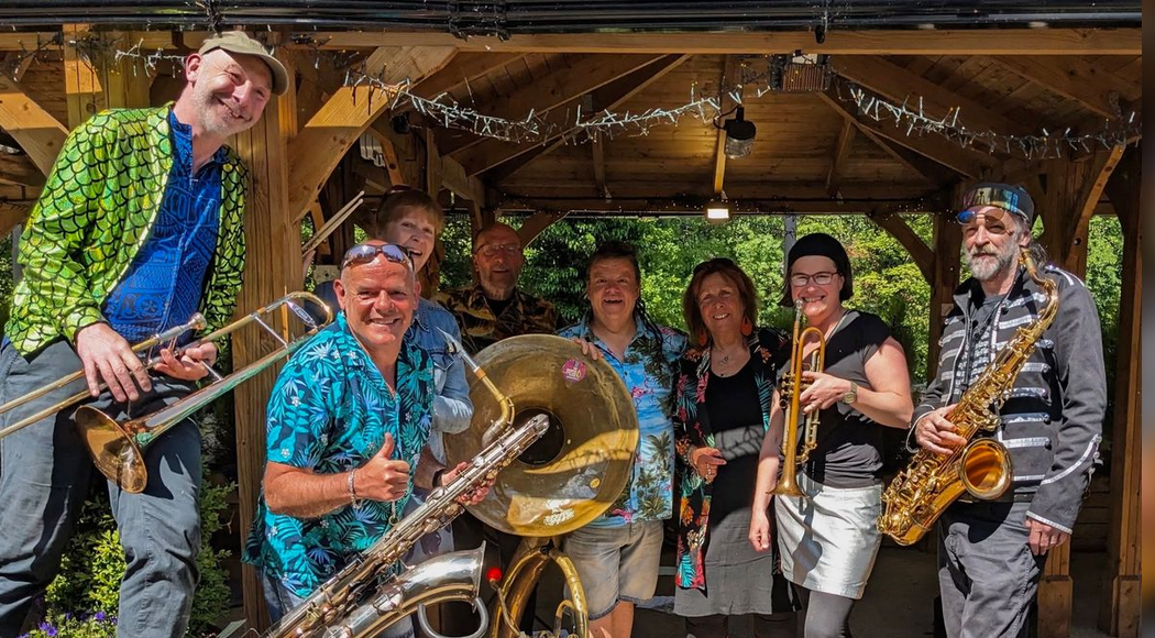 This is an image of the Homecoming Brass Band, consisting of 8 members in bright tops, holding their insruments.